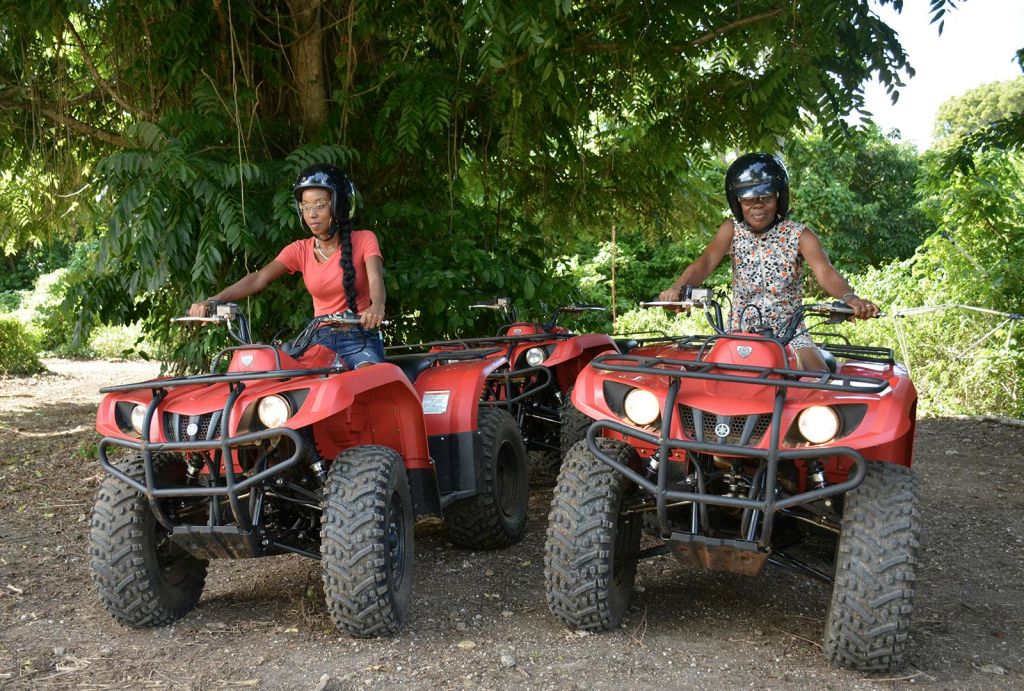 울창한 녹색 나무로 둘러싸인 흙길에서 빨간색 ATV를 타고 있는 헬멧을 쓴 두 사람.