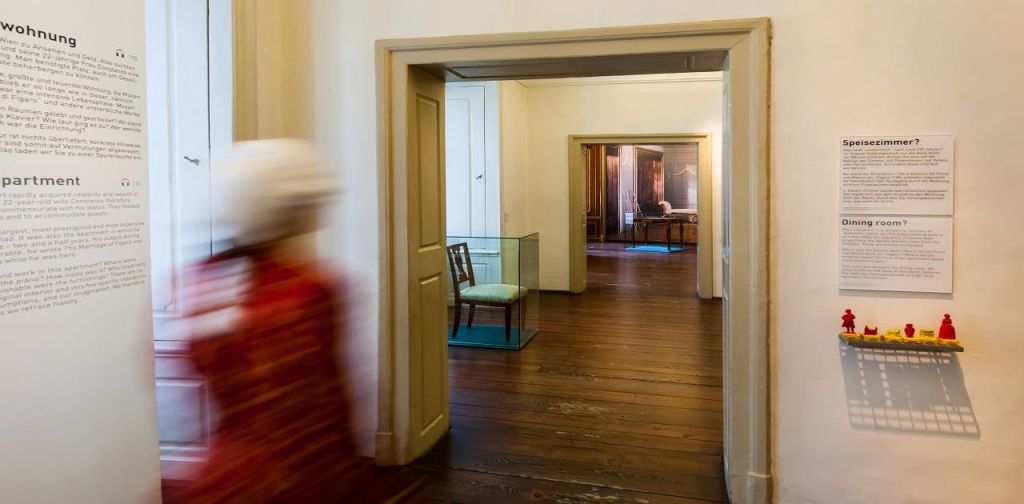 역사적인 건물에 있는 일련의 출입구로, 유리 케이스에 의자가 있고 흐릿한 사람이 지나가고 있습니다.