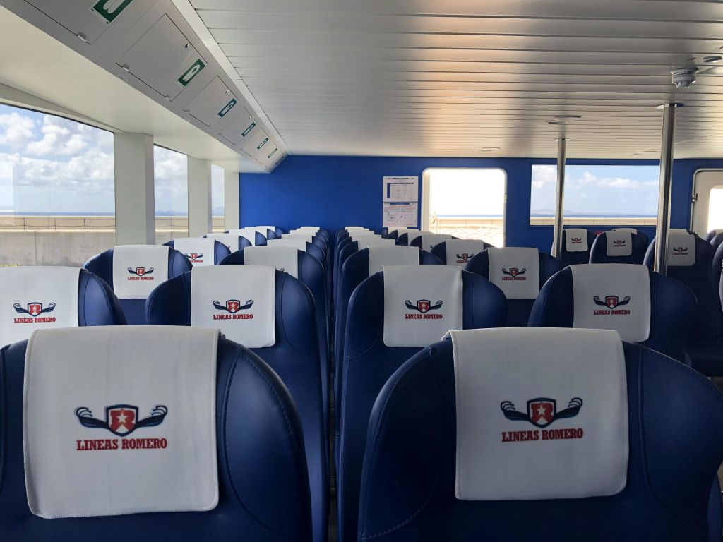 "LINEAS ROMERO" 로고가 표시된 흰색 커버가 있는 남색 좌석이 줄지어 있는 페리 내부.