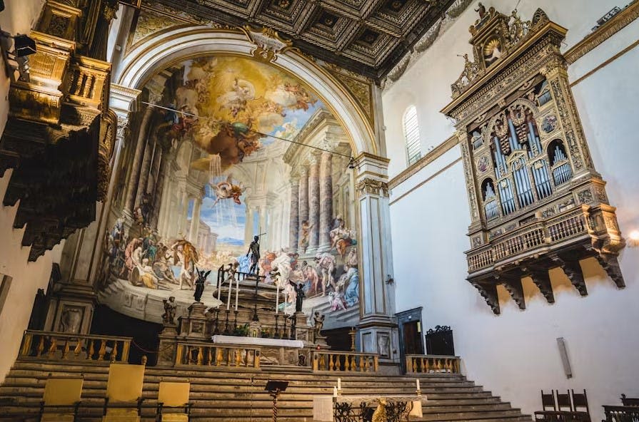 페인트칠된 아치형 천장, 화려한 제단, 정교한 조각, 오른쪽에 커다란 파이프 오르간이 있는 웅장한 교회 내부.