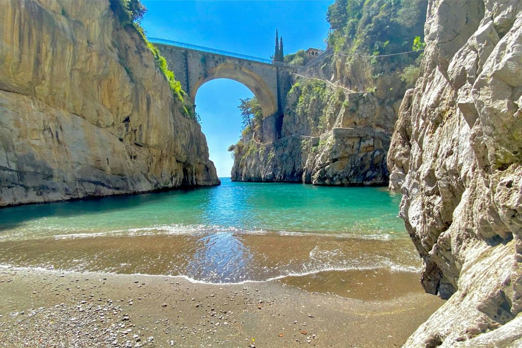 청록색 바다 위로 바위 절벽 사이로 펼쳐진 석조 아치 다리가 있는 아름다운 해안 전망, 모래 해변 근처.