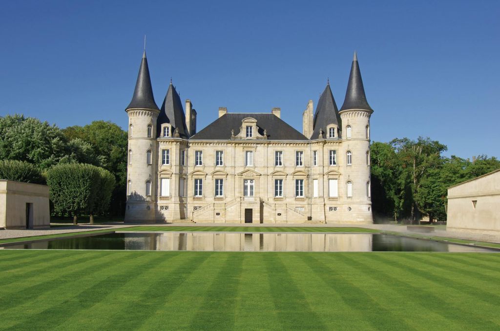 맑고 푸른 하늘 아래 잘 손질된 잔디밭과 나무로 둘러싸인 연못에 반사된 4개의 뾰족한 탑이 있는 석조 성.