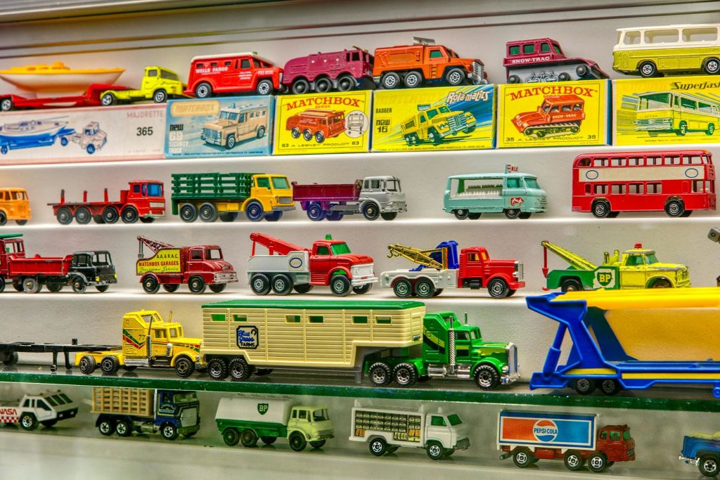 다채로운 포장 상자가 있는 선반에 배치된 매치박스 모델을 포함한 다양한 빈티지 장난감 자동차와 트럭의 전시.