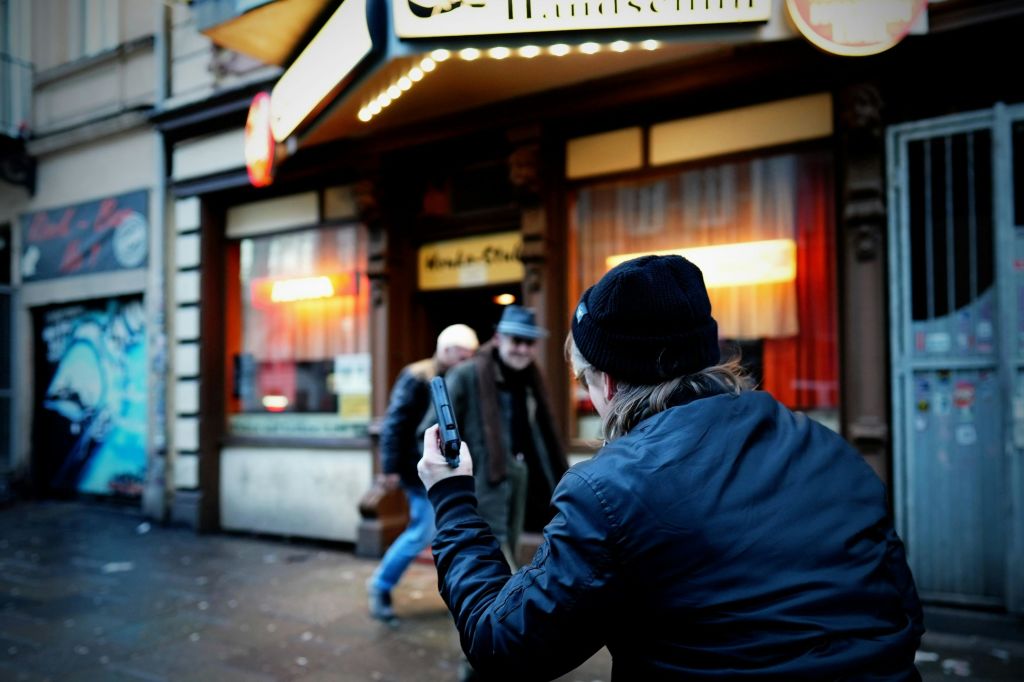 빨간색 커튼과 간판이 있는 밝은 점포 앞에서 두 남성을 촬영한 비니를 입은 사람.