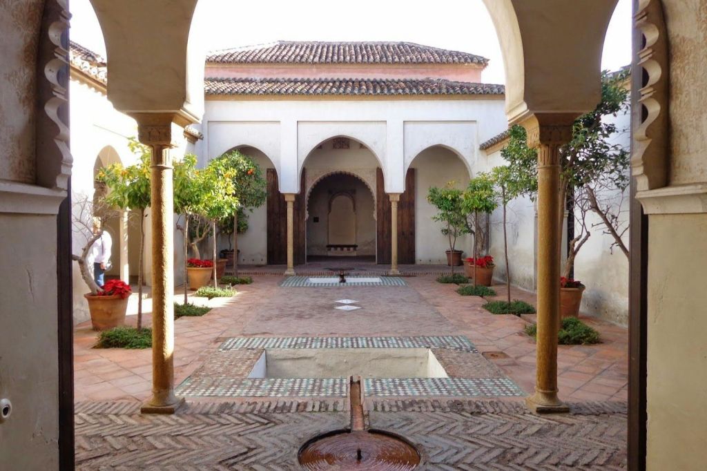 아치, 화분, 타일로 마감된 지붕 구조물 아래 타일로 마감된 통로로 둘러싸인 중앙의 물놀이를 즐길 수 있는 마당입니다.