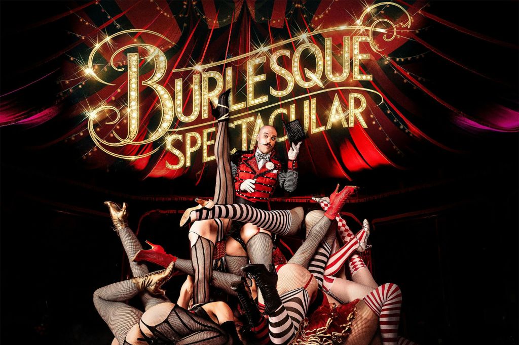 한 공연자가 줄무늬와 망사 스타킹을 입은 댄서들의 다리에 둘러싸인 "벌레스크 스펙타큘러 (Burlesque Spectacular)" 간판 아래에 서 있습니다.