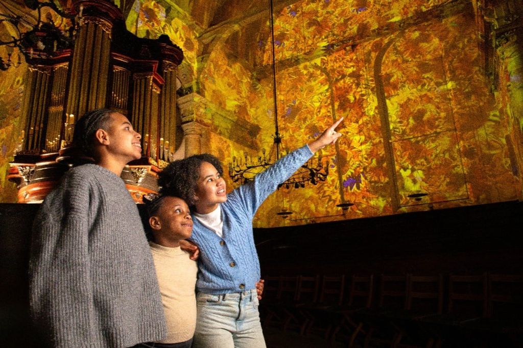 웅장한 실내 환경에서 다채롭고 빛나는 천장을 바라보며 세 사람이 함께 서 있습니다.