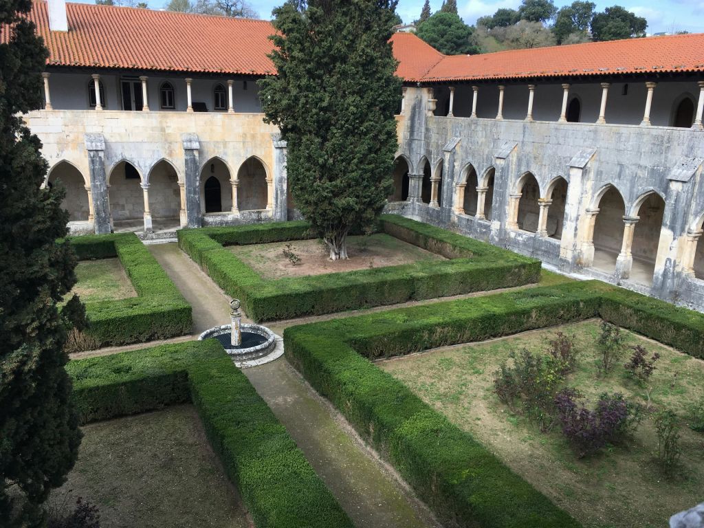 울타리를 다듬은 안뜰, 중앙 동상과 나무, 아치와 붉은 기와 지붕이 있는 고대 석조 회랑으로 둘러싸여 있습니다.