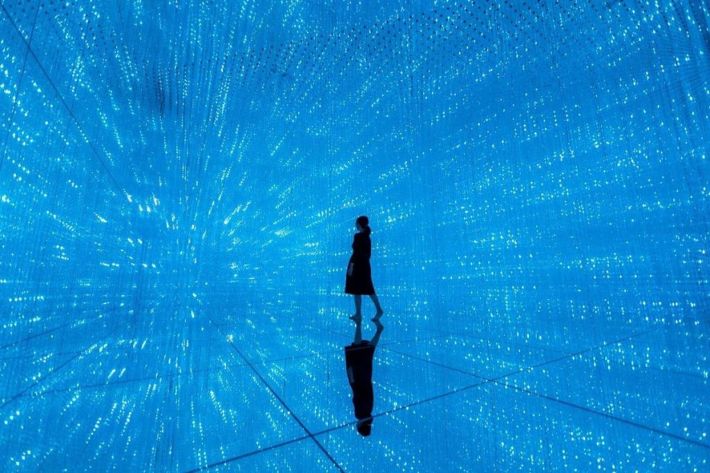 한 사람이 파란 불빛이 가득한 거울 방에 서서 끝없는 광선의 환상을 만듭니다.