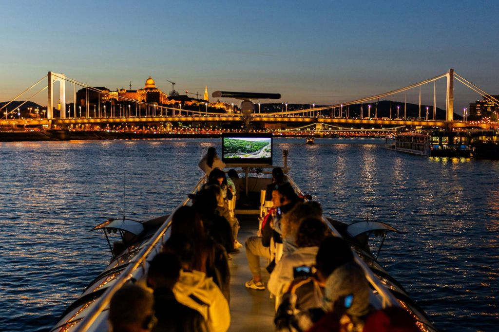 해질 무렵 보트에 앉은 사람들로, 도시 풍경이 조명을 받은 건물과 다리를 배경으로 펼쳐집니다.