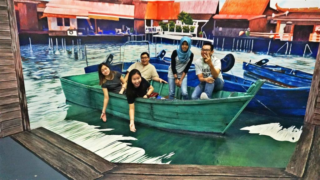 어촌 마을 수변을 닮은 그림이 그려진 한 장면 속에 5명이 초록색 나무 보트에 앉아 있습니다.