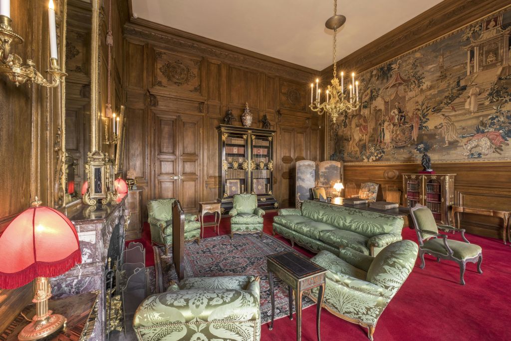 나무 패널 벽, 초록색 가구, 대형 책장, 화려한 샹들리에, 디테일한 태피스트리가 있는 고급스러운 객실입니다.