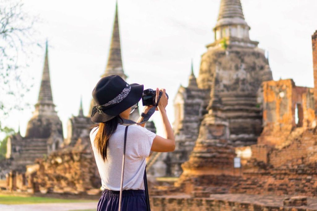 모자를 쓴 여성이 화창한 날 고대 사원 유적의 사진을 찍고 있습니다.