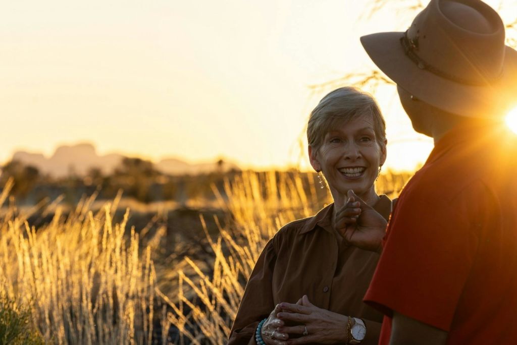 마른 잔디와 먼 풍경을 배경으로 석양을 바라보며 미소 짓고 이야기를 나누는 두 사람.