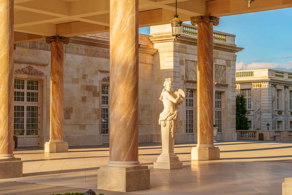 화려한 석조 건축물이 있는 햇살이 비치는 클래식 스타일의 안뜰에는 대리석 조각상이 기둥 사이에 서 있습니다.