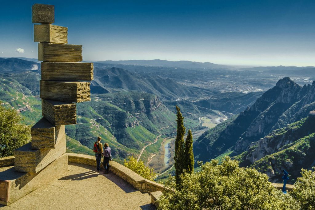구불구불한 강과 녹음이 우거진 광활한 산악 풍경이 내려다보이는 테라스에 두 사람이 서 있습니다.