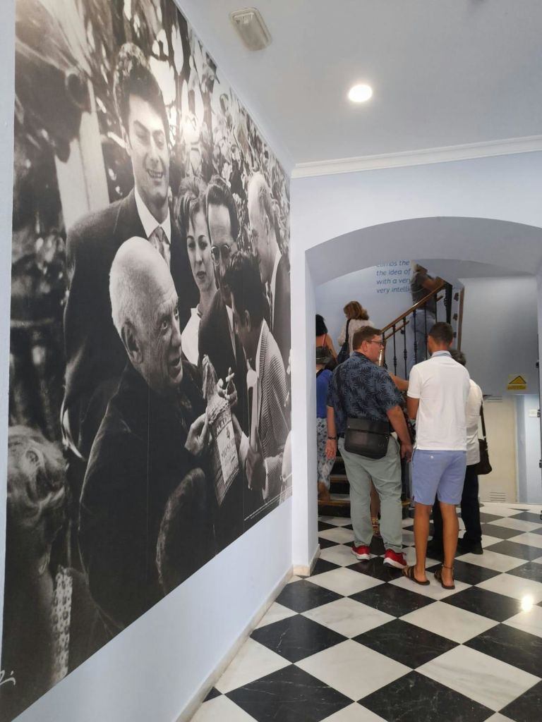 흑백 사진 속 나이가 많고 어린 사람들의 커다란 벽화 옆 계단을 오르는 사람들.