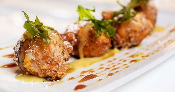 푸른 약초로 장식하고 소스를 뿌린 직사각형 흰색 접시에 담긴 튀긴 음식의 클로즈업.