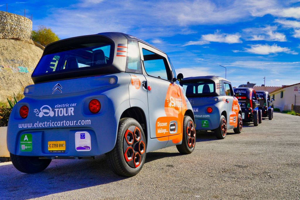 화창한 날 여러 대의 소형 전기 자동차가 연달아 주차되어 있으며, 각 차량에는 시티 투어 서비스에 대한 광고가 표시됩니다.