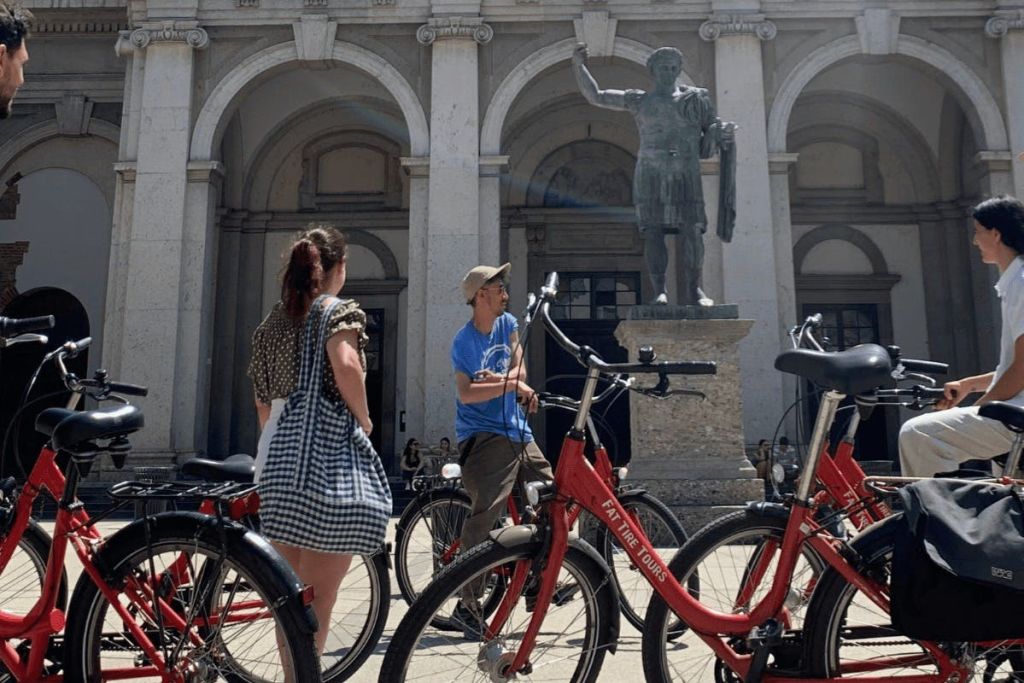 커다란 조각상과 아치형 건물 앞에 빨간색 자전거 근처에 서 있는 사람들.