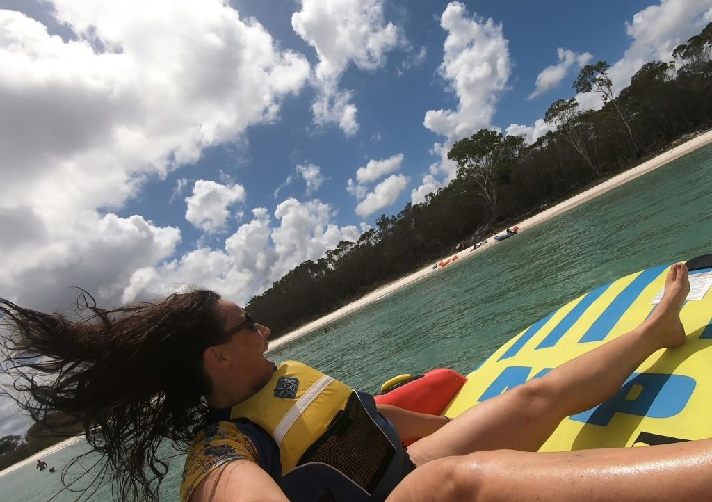 투명한 바다에서 다채로운 색상의 팽창식 뗏목에 노란색 구명조끼를 입고 모래 해변과 나무를 배경으로 활동하는 사람.