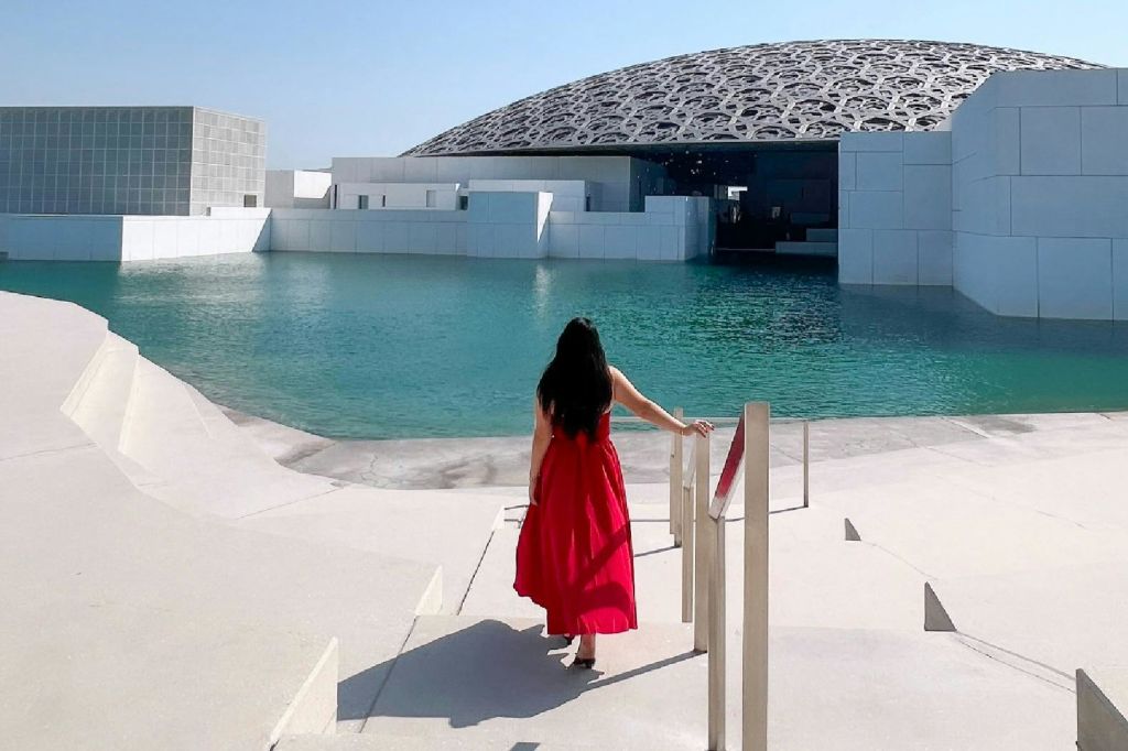 빨간 드레스를 입은 한 여성이 난간 근처에 서서 맑고 푸른 하늘 아래 돔형 건물을 내려다보고 있습니다.