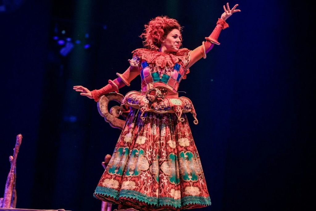 화려하고 정교한 의상을 입은 공연자가 어두운 배경을 배경으로 무대에서 극적인 포즈를 취하고 있습니다.