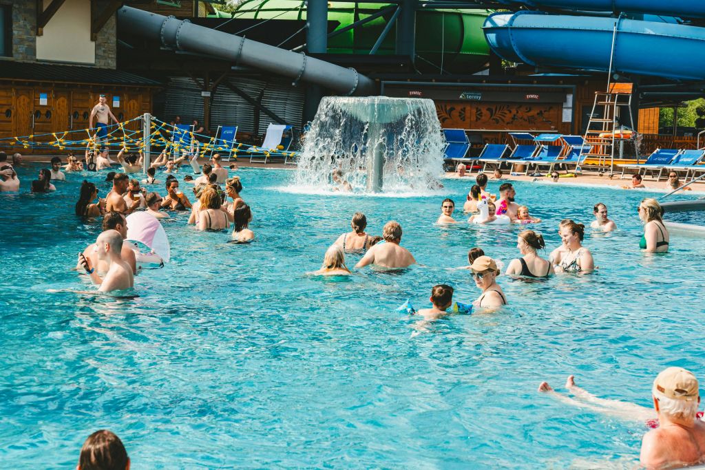 사람들로 붐비는 수영장은 중앙 폭포 주변에 자리 잡고 있습니다. 백그라운드에서 즐기는 워터슬라이드