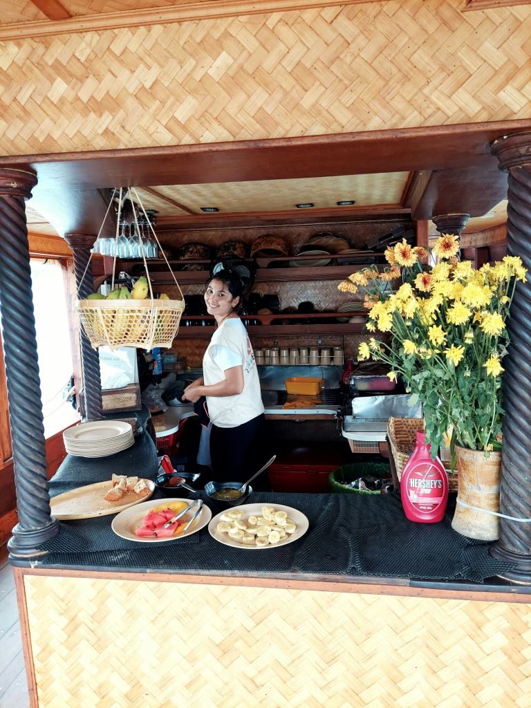 꽃과 과일로 둘러싸인 대나무 인테리어가 돋보이는 주방의 한 여성이 바구니가 걸린 카운터에서 음식을 준비하고 있습니다.