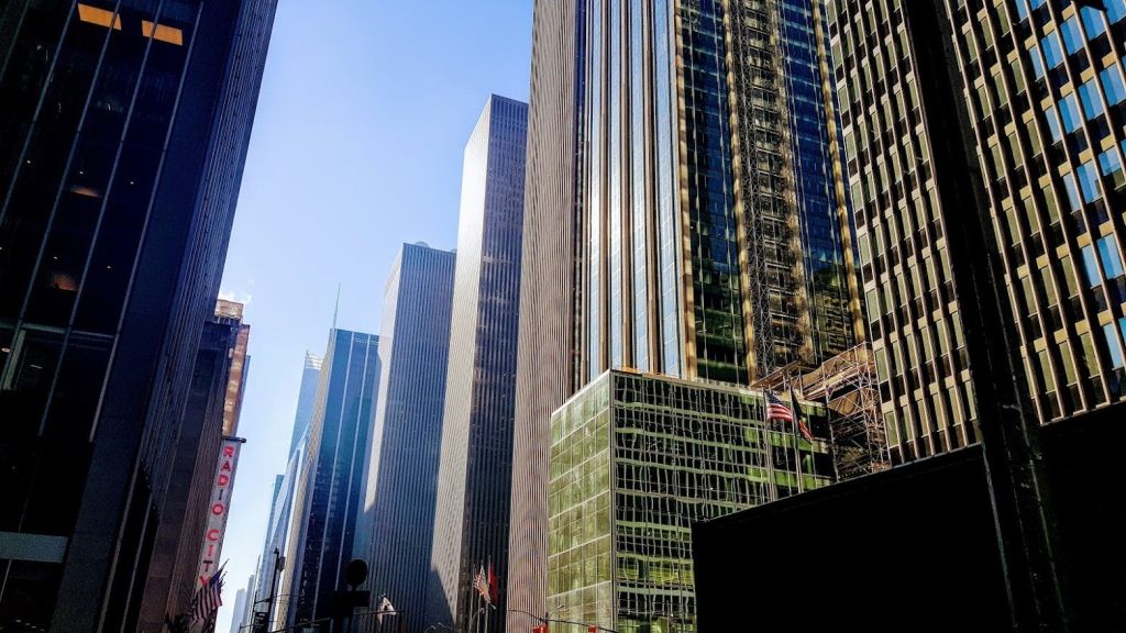 맑고 푸른 하늘 아래 반사창문이 있는 키가 큰 현대적인 고층 건물로, 전면에 미국 국기가 보입니다.