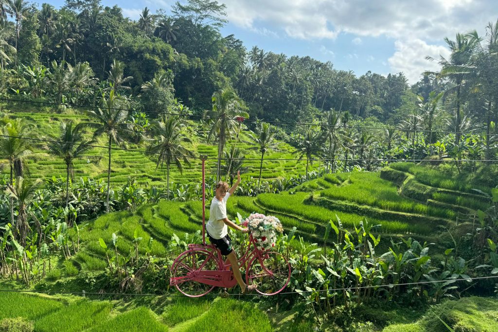 U Fun Field 공원의 계단식 논 위에서 스카이바이크를 타고 자전거를 타며 카메라를 향해 손을 흔들고 미소를 짓는 남성