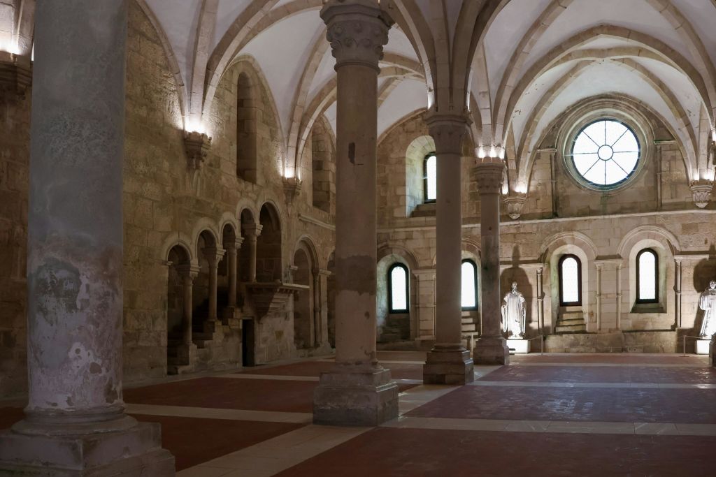 아치, 기둥, 아치형 천장, 자연광이 비추는 골방에 있는 동상이 있는 유서 깊은 석조 홀입니다.