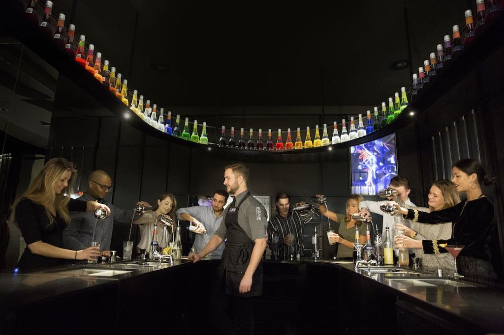 바텐더가 현대적인 바 환경에서 다채로운 색상의 병 아래에서 음료를 믹싱하는 사람들을 돕고 있습니다.