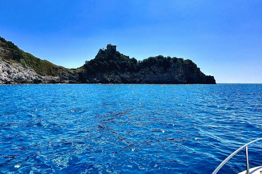 바위 같은 해안선이 나무로 뒤덮인 작은 섬, 맑은 하늘 아래 밝고 푸른 바다에서 바라본 성.