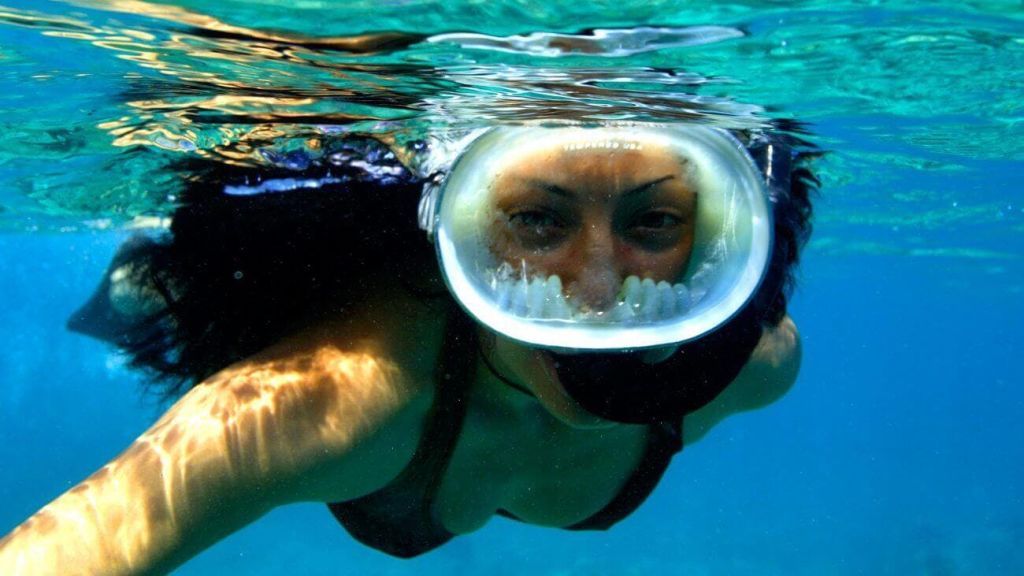 맑고 푸른 물로 둘러싸인 전면 마스크를 착용하고 수중에서 스노클링을 즐기는 사람.