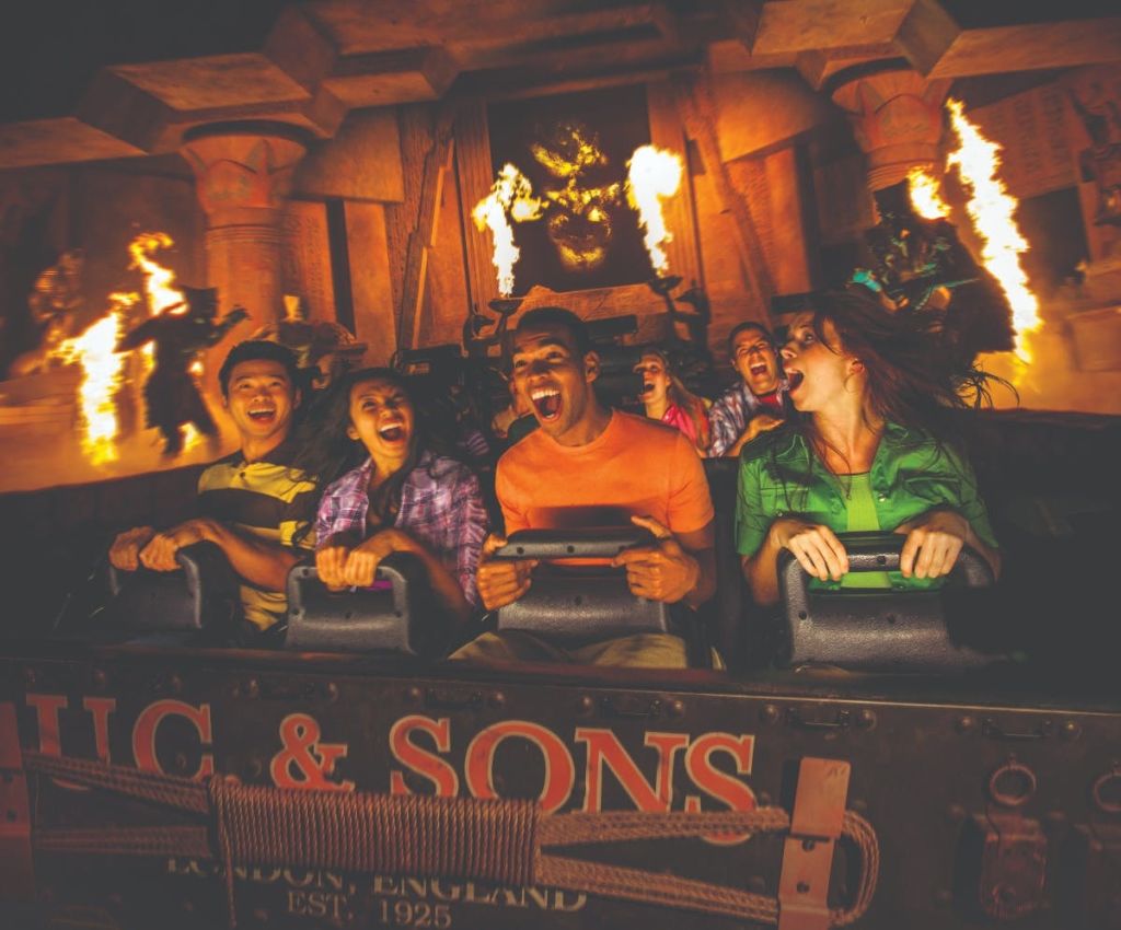 불길과 기둥, 커다란 조각상을 배경으로 테마파크에서 비명을 지르는 사람들.