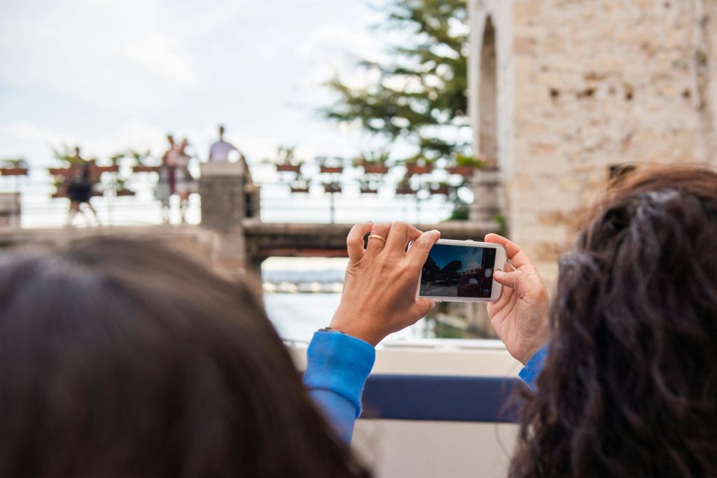 스마트폰을 들고 사람과 화분이 놓인 다리의 사진을 찍는 사람, 다른 사람이 지켜보는 사람.