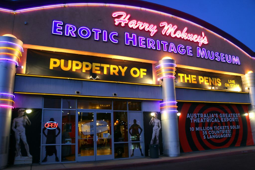 "Harry Mohney's Erotic Heritage Museum" 과 "Puppetry of the Penis" 를 읽는 네온 사인이 있는 박물관 입구에 마네킹과 "Open" 사인이 있습니다.