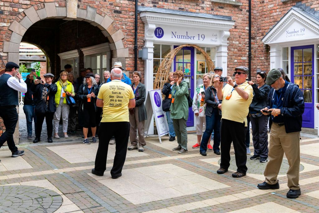투어 그룹이 벽돌로 된 아치형 통로와 '19번' 이라고 적힌 상점 앞에 서면 노란 셔츠를 입은 가이드가 안내합니다.
