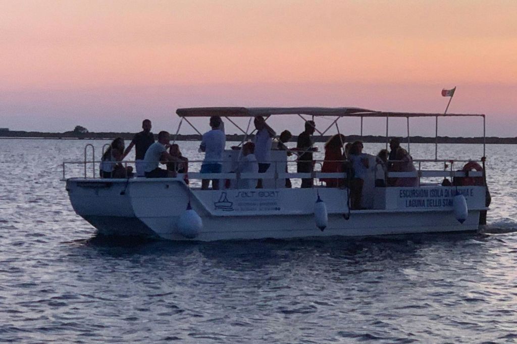 해가 질 무렵 분홍색 주황색 하늘을 배경으로 잔잔한 물 위에 떠 있는 흰색 투어 보트를 탄 사람들.