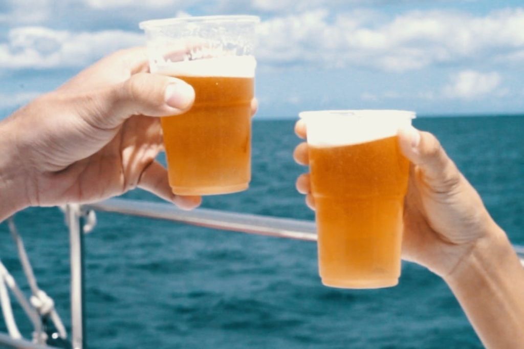 바다와 푸른 하늘을 배경으로 맥주로 가득 찬 플라스틱 컵을 들고 있는 두 손.