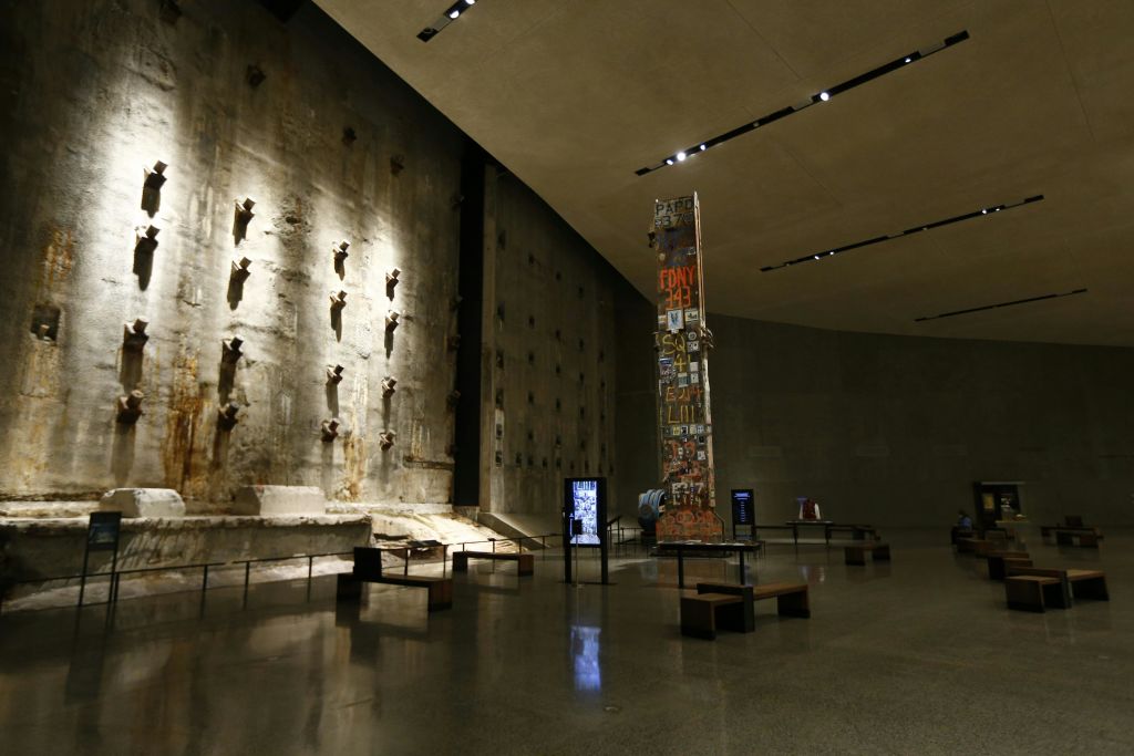 광택이 나는 바닥에 커다란 콘크리트 벽, 물품으로 덮인 높은 기둥, 벤치, 전시 키오스크가 있는 박물관 전시관입니다.