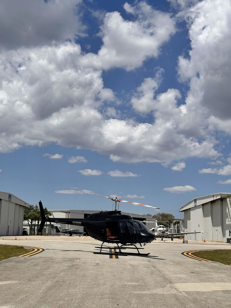 검은 헬리콥터가 두 개의 격납고 사이의 활주로에 앉아 있습니다.