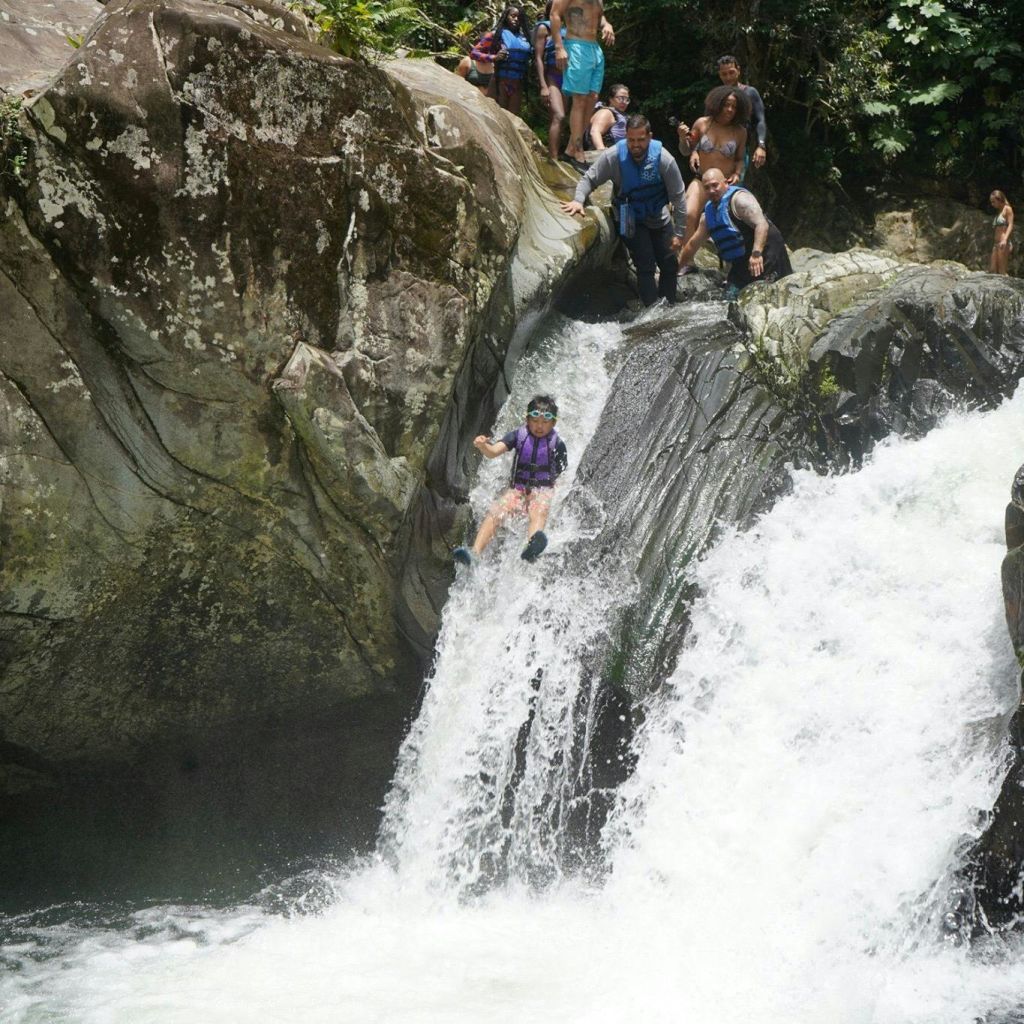 한 사람이 폭포를 따라 미끄러지듯 내려가고, 한 무리가 바위 위에서 바라보고 있습니다.