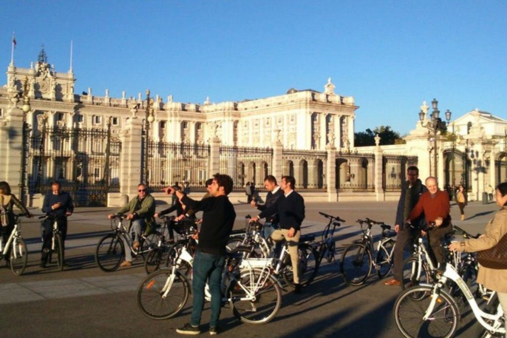 맑은 날 커다란 대문이 있는 화려하고 하얀 건물 앞에서 자전거를 타는 사람들입니다.