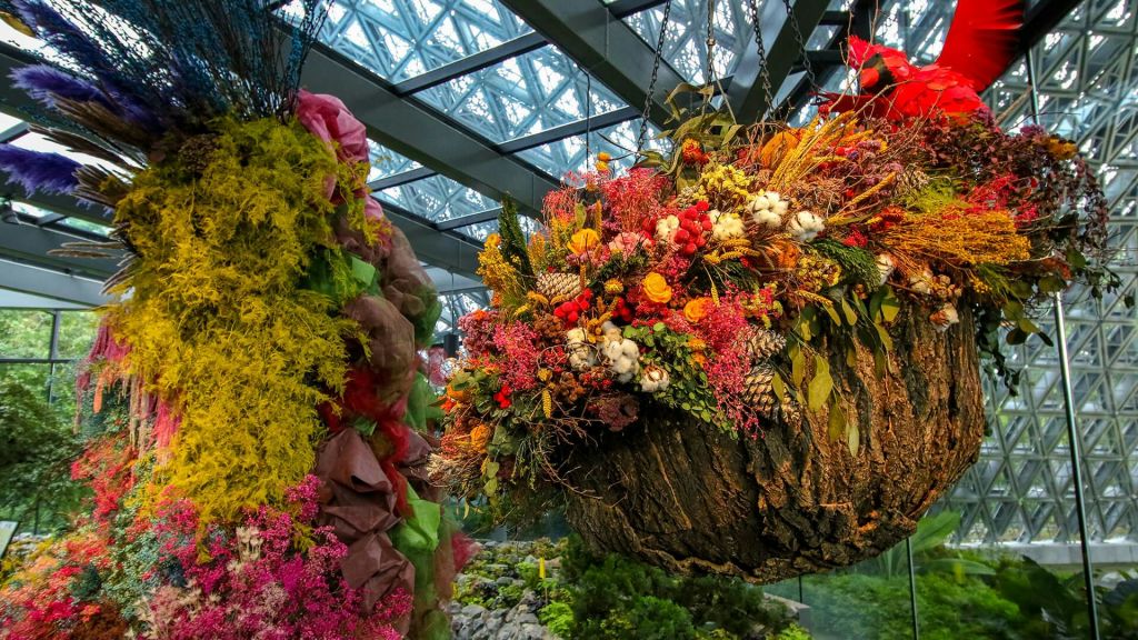 유리 지붕이 있는 온실에 밝은 색상의 꽃과 단풍이 있는 꽃꽂이를 걸고 있습니다.