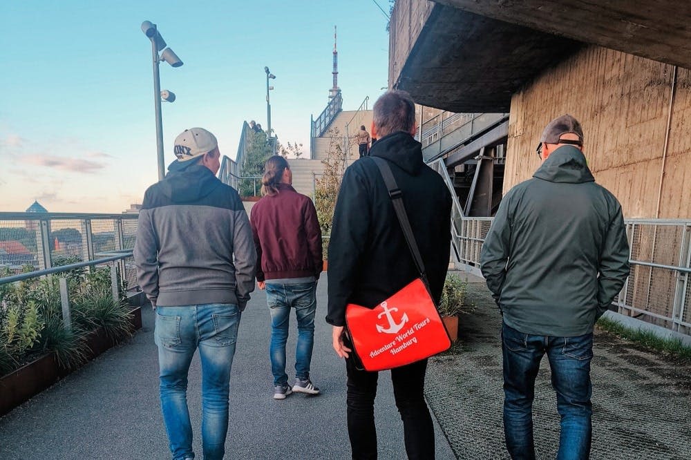 건물 옆의 높은 통로를 따라 걷는 네 명의 사람. 한 사람이 빨간색 숄더백을 들고 있습니다.