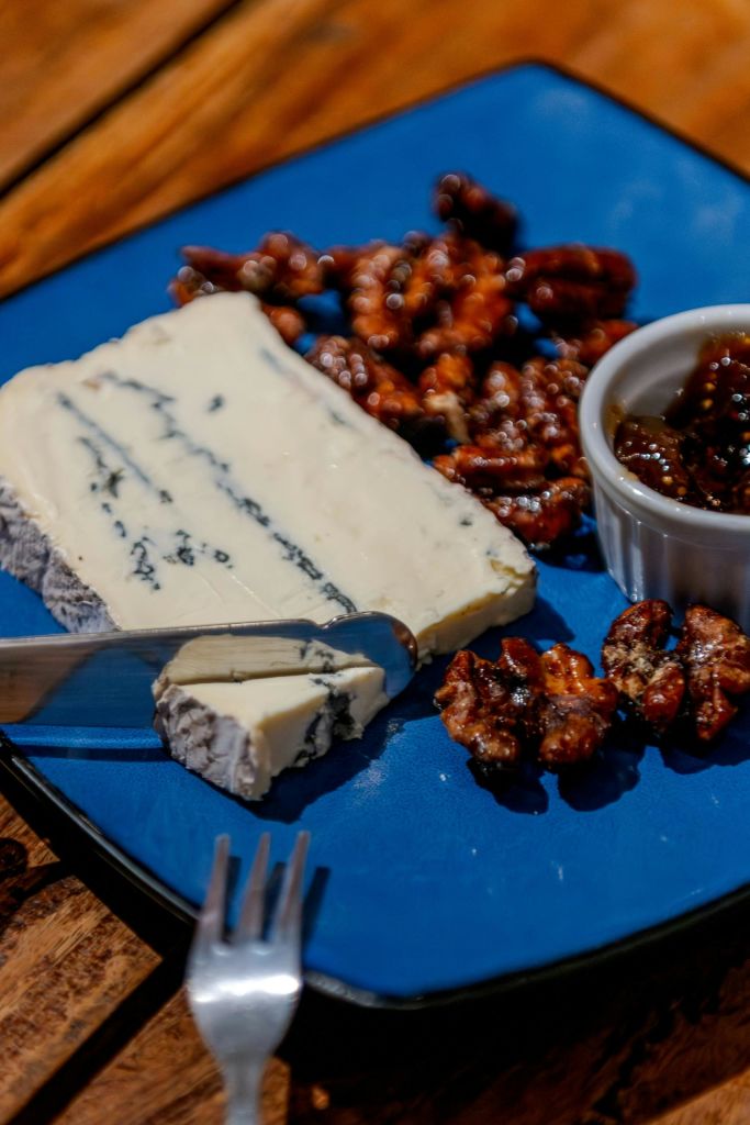 근처에 블루 치즈, 사탕 견과류, 작은 젓갈이 담긴 접시와 칼과 포크가 있습니다.