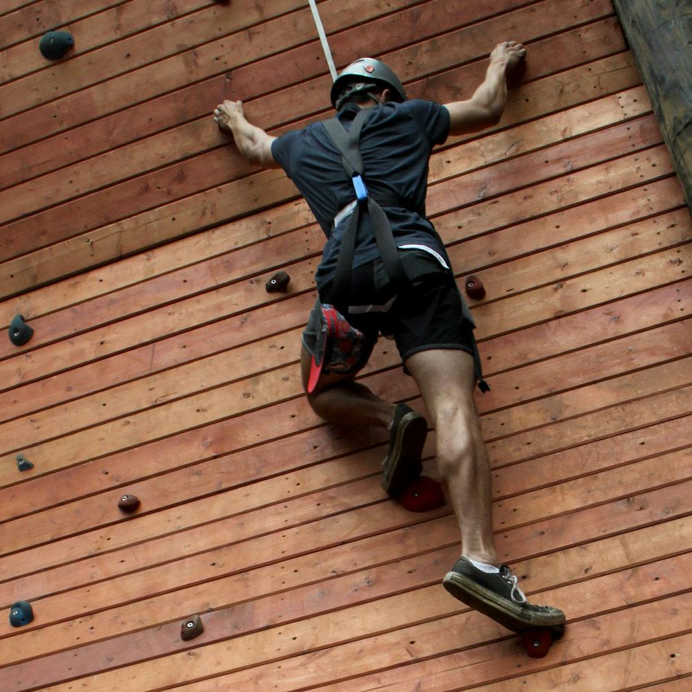 손잡이가 달린 나무 벽을 등반하는 헬멧과 하네스를 착용한 사람.
