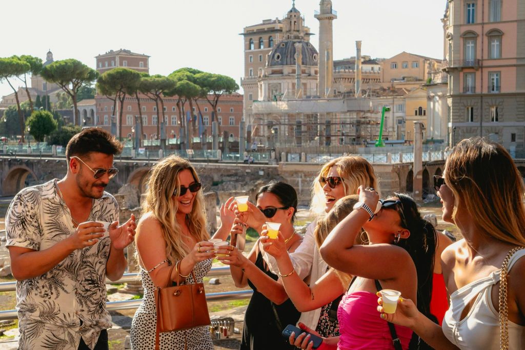 역사적인 건물과 나무를 배경으로 야외에서 음료를 즐기는 사람들의 모임.